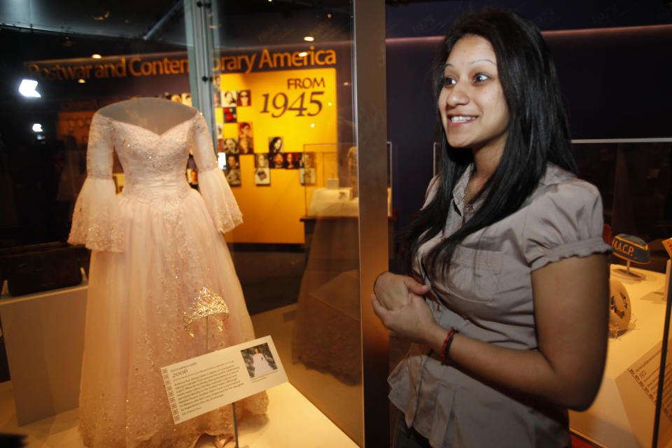 Singer Natalia Flores, 20, of Chicago, stands next to her Quinceanera dress from 2006 that is on display as part of the new exhibit, "American Stories," at the Smithsonian National Museum of American History in Washington, on Wednesday, April 11, 2012. The National Museum of American History will open a new exhibit featuring iconic objects from pop culture along with objects dating back to the Pilgrims' arrival in 1620. "American Stories" will be a new chronology of U.S. history from the first encounters of Europeans and Native Americans to the 2008 presidential election. (AP Photo/Jacquelyn Martin)