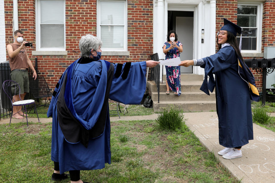 George Washington University graduate Catalina Perez (R) receives a paper copy of her diploma from neighbor Paula Lytle as they keep a social distance at a surprise graduation party for Perez, who completed her undergraduate studies in International Affairs across the span of ten years only to miss her commencement due to the coronavirus disease (COVID-19) outbreak in Washington, U.S., May 17, 2020. REUTERS/Jonathan Ernst     TPX IMAGES OF THE DAY