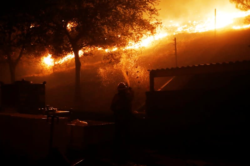 A firefighter defends a structure against approaching flames while battling the Kincade fire in Geyserville, California