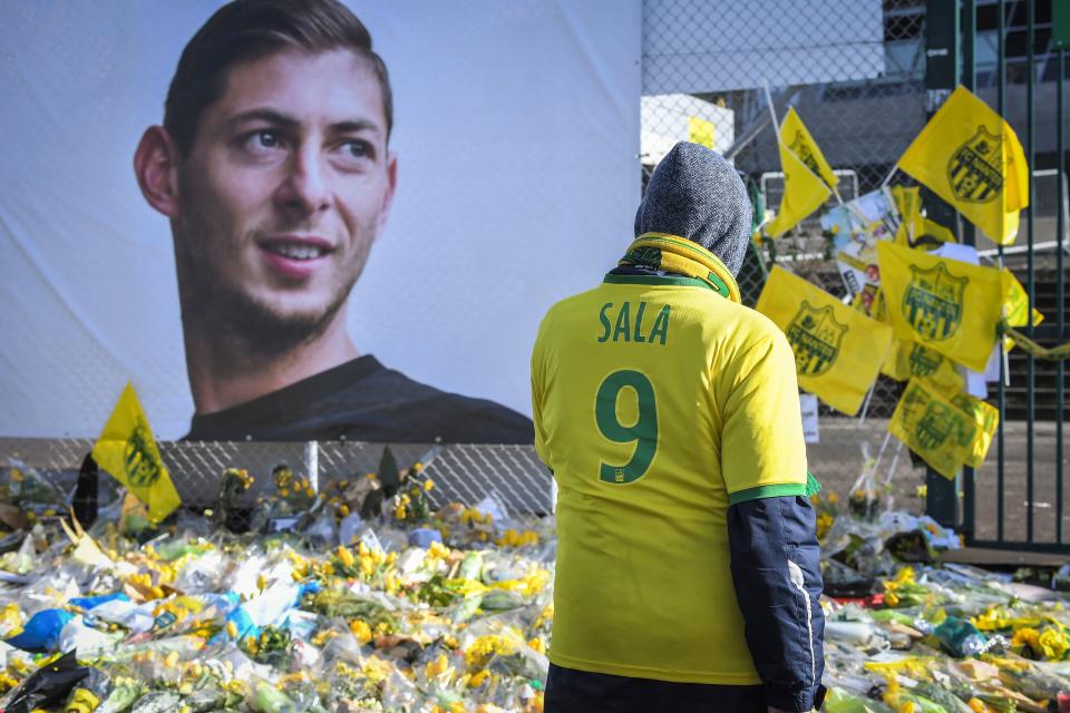 Supporters pay tribute and look at yellow flowers displayed in front of the portrait of Argentinian forward Emiliano Sala at the Beaujoire stadium in Nantes, on February 10, 2019. - FC Nantes football club announced on February 8, 2019 that it will freeze the #9 jersey as a tribute to Cardiff City and former Nantes footballer Emiliano Sala who died in a plane crash in the English Channel on January 21, 2019. (Photo by LOIC VENANCE / AFP)        (Photo credit should read LOIC VENANCE/AFP/Getty Images)