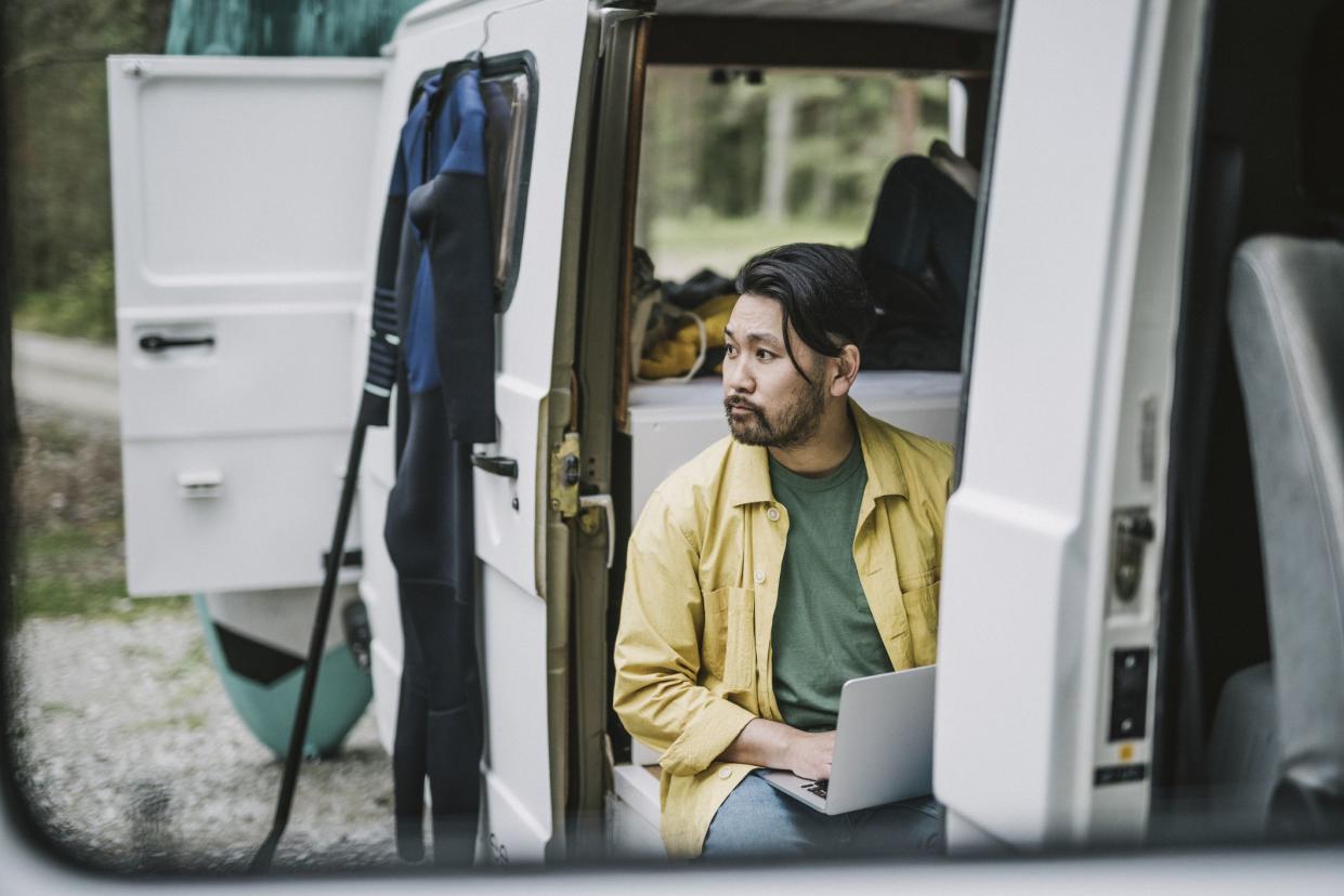 Japanese man working on laptop, while sitting in his mini van.