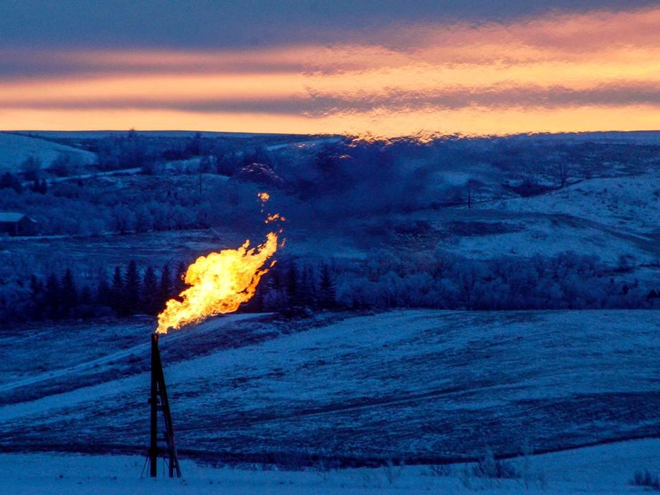 gas flare from oil well tower in north dakota hills at sunset