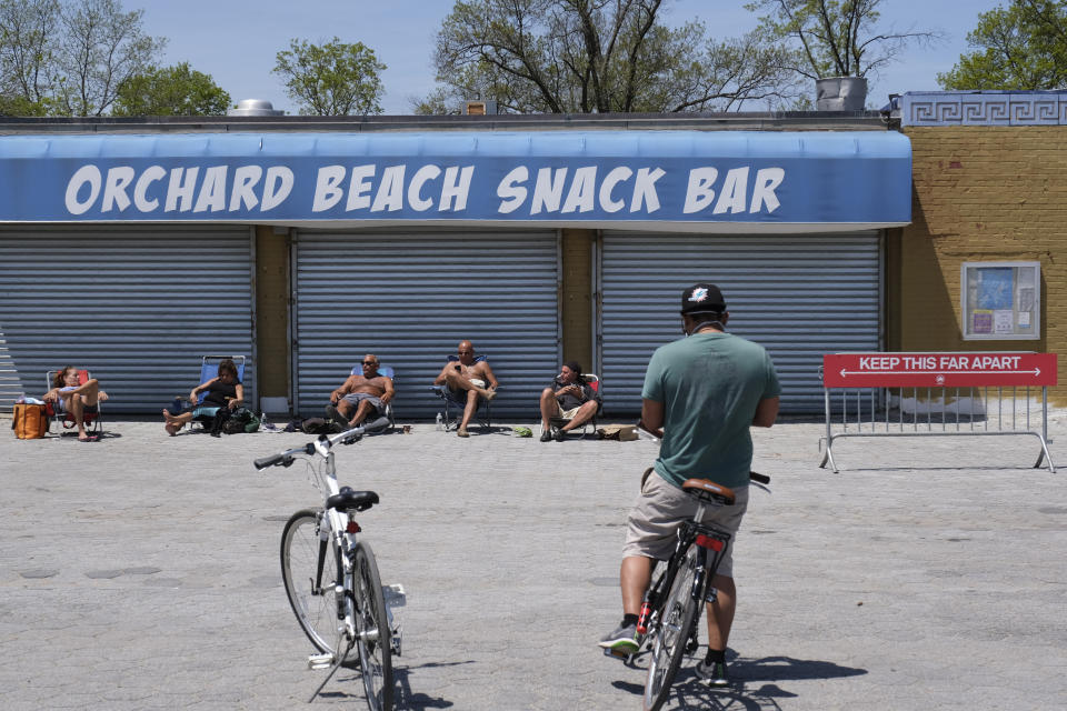 People take in the sun and relax in front of a closed snack bar at Orchard Beach in the Bronx borough of New York, Sunday, May 17, 2020. Parks, boardwalks and beaches attracted some crowds this weekend, though city beaches aren't officially open and won't be for the upcoming Memorial Day weekend. New York City Mayor Bill de Blasio said the city's beaches could be closed off completely to public access if people don't follow social distancing rules. Fencing is being installed at entrance ways and could be rolled out if beaches — meant now only for nearby residents to get some exercise — get overcrowded or people violate swimming bans, he said. (AP Photo/Seth Wenig)