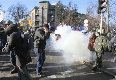 Anti-government protesters react during a rally, as smoke is seen in the background, near the Vekhovnaya Rada building, Ukraine's house of parliament, in Kiev, February 18, 2014. REUTERS/Gleb Garanich