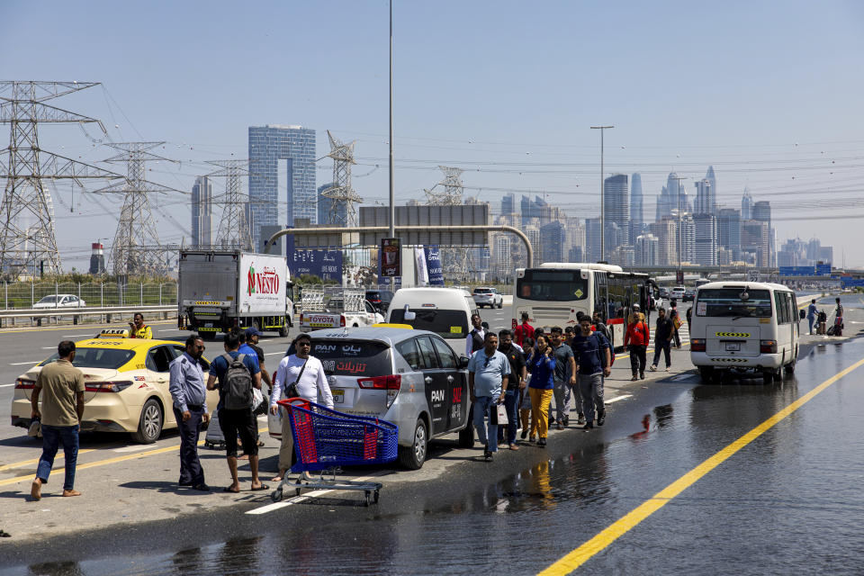 People wait for transportation amidst floodwater caused by heavy rain on Sheikh Zayed Road highway in Dubai, United Arab Emirates, Thursday, April 18, 2024. The United Arab Emirates attempted to dry out Thursday from the heaviest rain the desert nation has ever recorded, a deluge that flooded out Dubai International Airport and disrupted flights through the world's busiest airfield for international travel. (AP Photo/Christopher Pike)