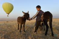 A Kyrgyz boy pets a donkey as other people launch a balloon at sunset outside Tash-Dyobyo village, 12 kilometers (7,5 miles) south of Bishkek, Kyrgyzstan, Saturday, Oct. 17, 2020. The political turmoil that has gripped Kyrgyzstan hasn’t reached this quiet village in the mountains near the capital, where residents talk about the country’s feuding elites with resignation and disdain.(AP Photo/Vladimir Voronin)