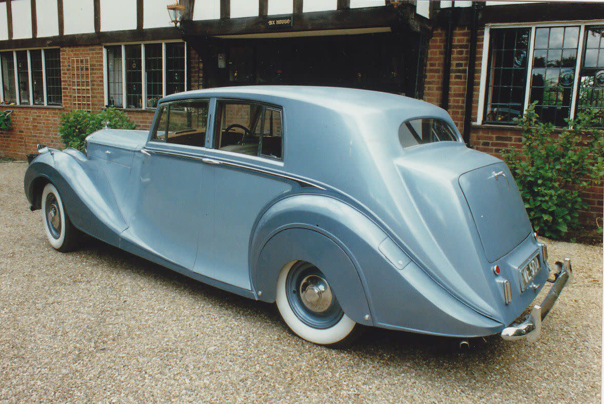 Light blue 1950 Bentley Mark VI parked on gravel driveway in front of a tudor house.