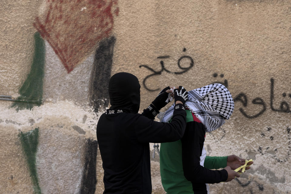 A Palestinian youth assists his friend to tie his scarf before a weekly protest in the West Bank town of Kfar Qaddum, Friday, Jan. 13, 2023. (AP Photo/ Maya Alleruzzo)