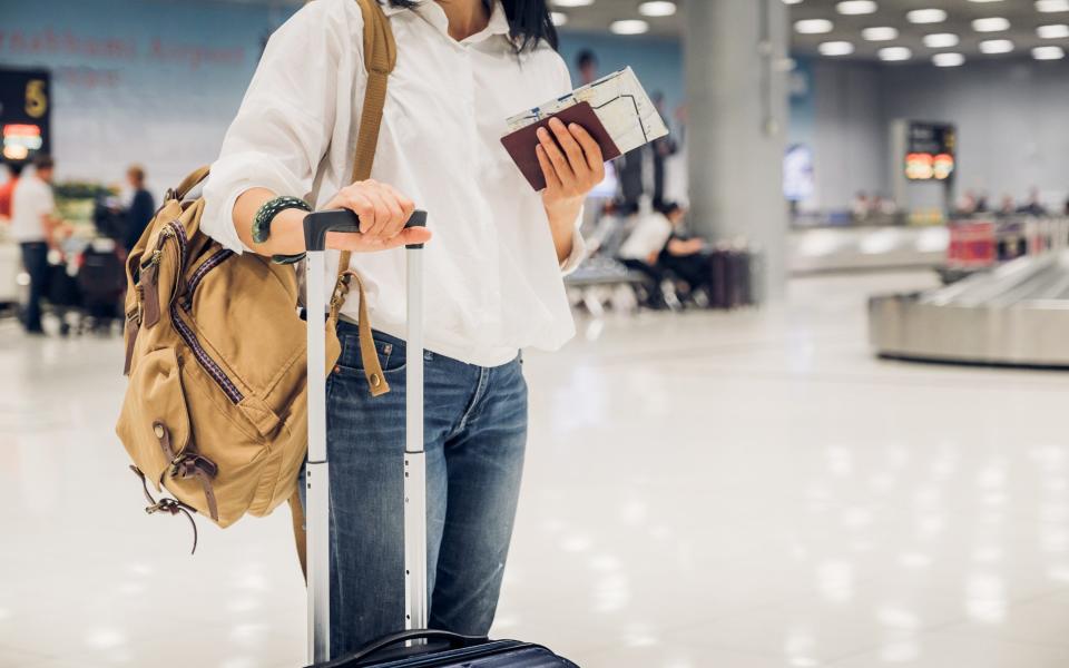 Woman backpacker holding passport and map with suitcase standing at check in baggage at airport terminal,traveler concept.