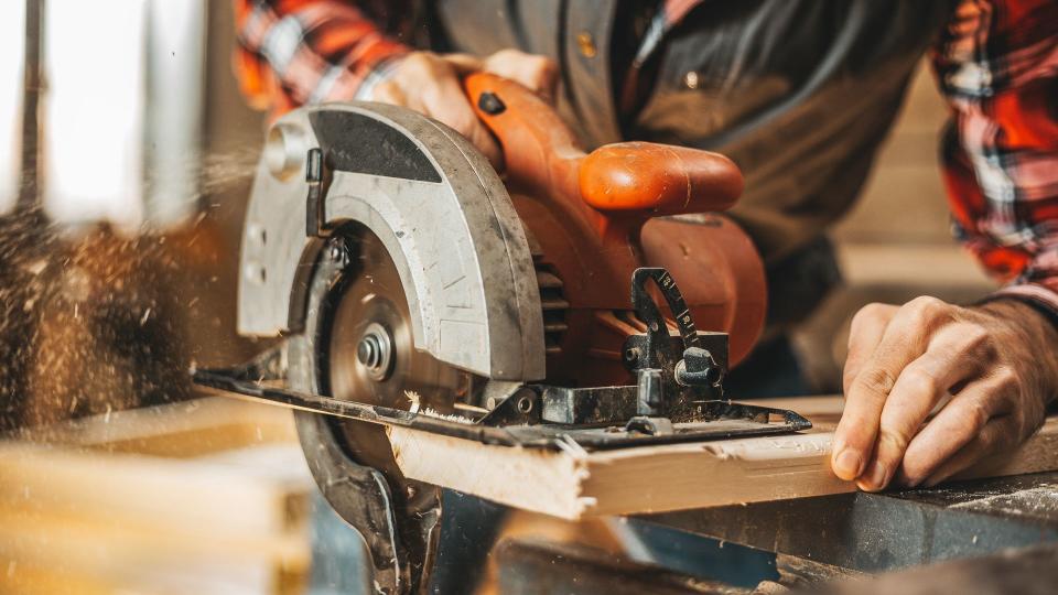 Carpenter cutting plank by circular saw in him workshop.