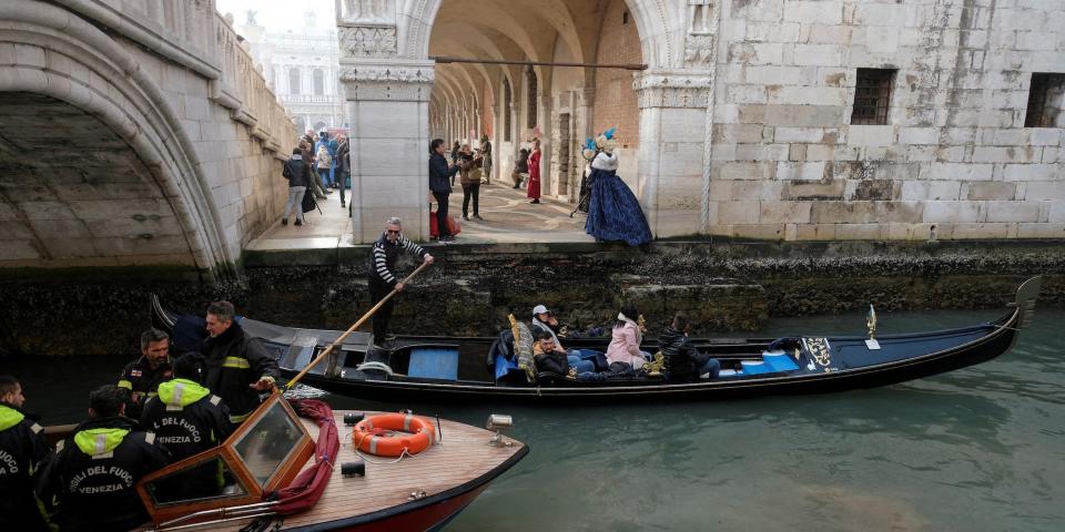 A fire boat and a gondola in Venice, about to go under a bridge, with the water level very low, on February 17 2023.