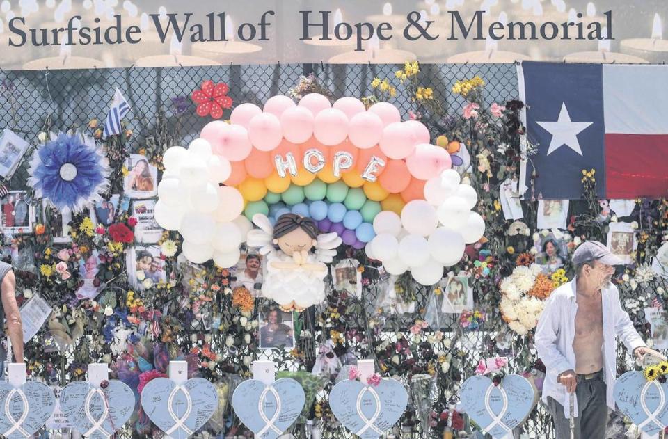 Wooden hearts with the names of victims are erected along side the photos, flowers, and other memorial items as visitors walk through the memorial site of the partial collapse of the Champlain Towers South in Surfside, on Sunday, July 11, 2021.