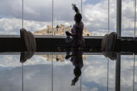 Hotel worker Mailinda Kaci cleans the windows in a restaurant area at the Acropolian Spirit Hotel in central Athens as the ancient Acropolis is seen in the background, on Monday June 1, 2020. Lockdown restrictions were lifted on non-seasonal hotels Monday as the country prepares to start its tourism season on June 15. (AP Photo/Petros Giannakouris)