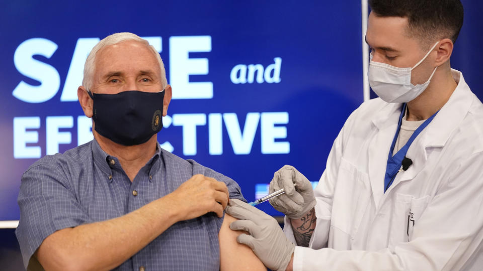 A health care working gives an injection into Mike Pence's left arm, both wear face masks.
