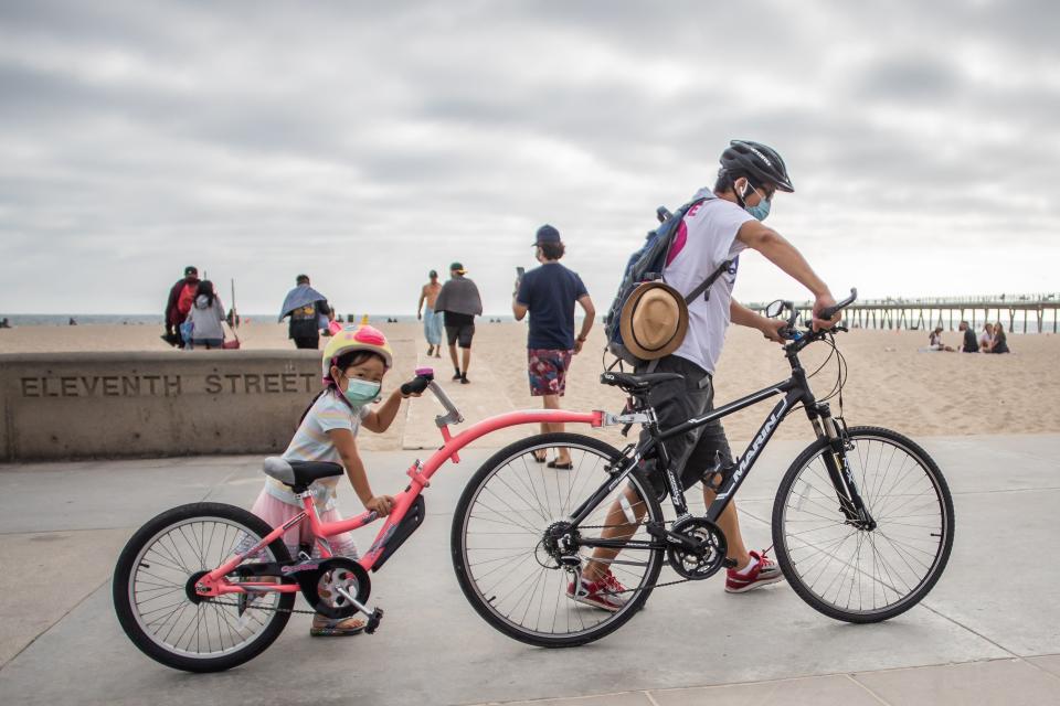 A girl and her father wear facemasks while they push their bikes in Hermosa Beach, Los Angeles, California, on July 14, 2020. - California's Governor Gavin Newsom announced a significant rollback of the state's reopening plan on July 13, 2020 as coronavirus cases soared across America's richest and most populous state. (Photo by Apu GOMES / AFP) (Photo by APU GOMES/AFP via Getty Images)