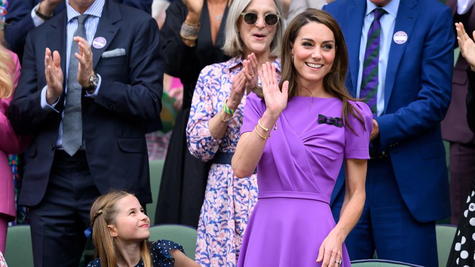 Kate Middleton macha w fioletowej sukience, a księżniczka Charlotte przygląda się temu z trybun.