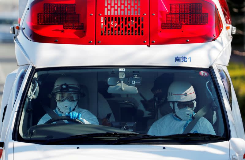 Ambulance workers in protective gears drive an ambulance which is believed to be carrying a person who was transferred from cruise ship Diamond Princess after ten people were tested positive for coronavirus, at a maritime police's base in Yokohama