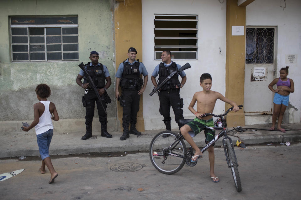 Police officers chat as they stand guard next to young residents at the Mandela shantytown, part of the Manguinhos slum complex, after attacks to their Pacifying Police Unit posts in Rio de Janeiro, Brazil, Friday, March 21, 2014. Rio de Janeiro police say suspected drug gang members on Thursday night attacked three police slum outposts and burned one of them. Officials say they'll ask for elite Brazilian federal police to help quell a wave of violence in supposedly pacified slums. (AP Photo/Felipe Dana)