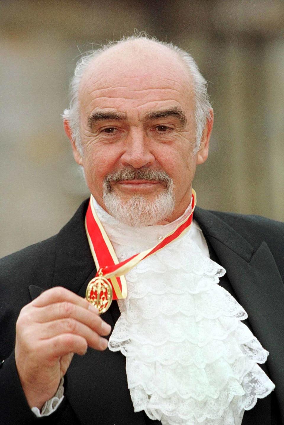 Homme avec une médaille, vêtu d'un costume et d'une cravate à volants, souriant à la caméra