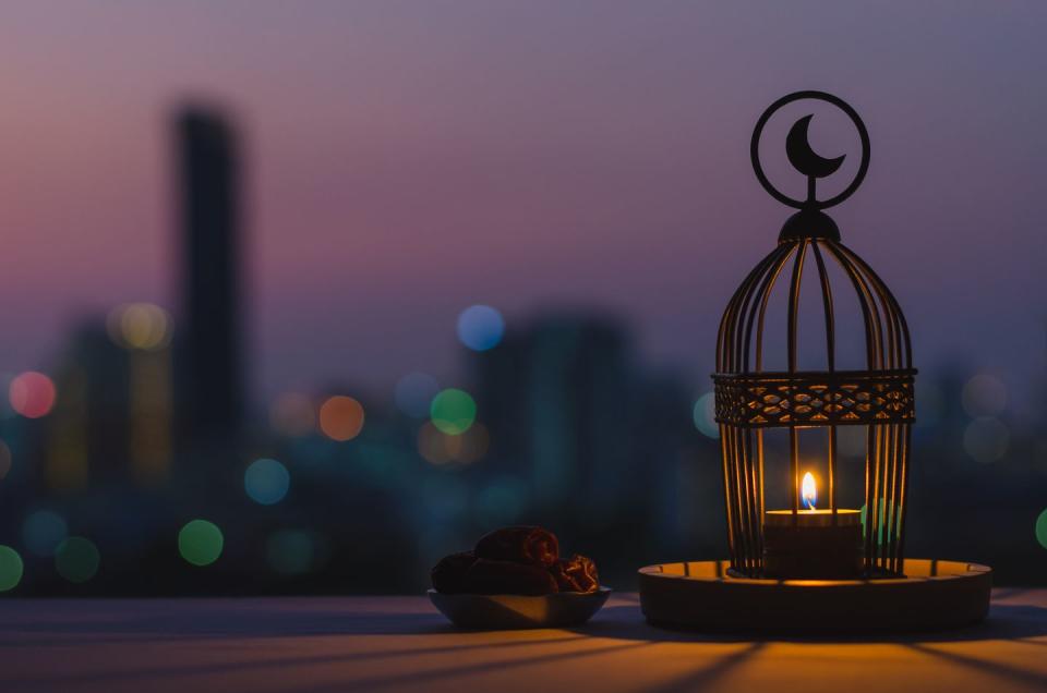 lantern that have moon symbol on top and small plate of dates fruit with dusk sky and city bokeh light background