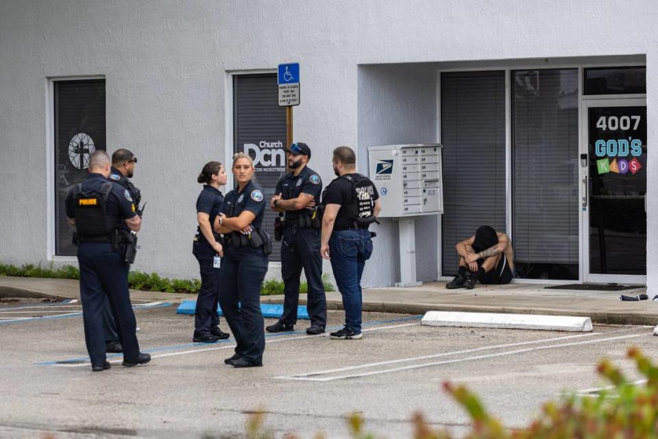 City of Doral police officers stand by a man sitting in front of DCN Church off 4005 NW 79th Avenue after a shooting on Friday, July 5, 2024. One person died in the shooting, and two people were wounded, police said.