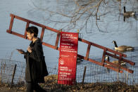 A pedestrian walks past an ice rescue ladder station as geese swim nearby, Monday, Jan. 30, 2023, at Central Park in the Manhattan borough of New York. Since the start of winter in December, there hasn't been any measurable snowfall in the city. The last time it took this long before snow lingered on the ground in the wintertime was 1973, when New Yorkers had to wait until Jan. 29. (AP Photo/John Minchillo)