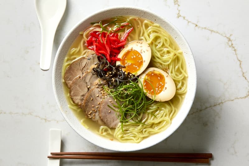 overhead shot of a white textured bowl with tonkotsu ramen, with a soup spoon to the left and chopsticks below the bowl.