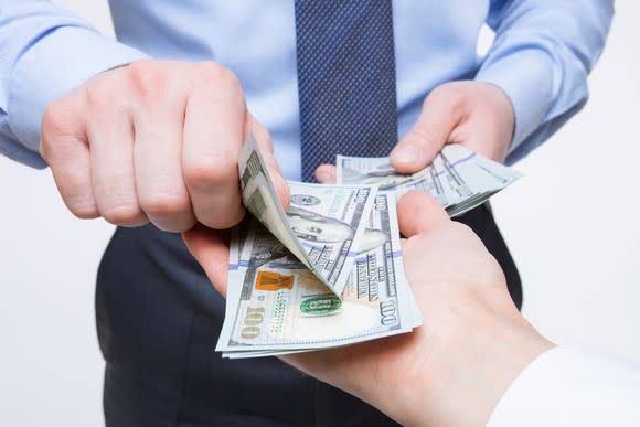 A man counting out $100 bills into another man's hand.