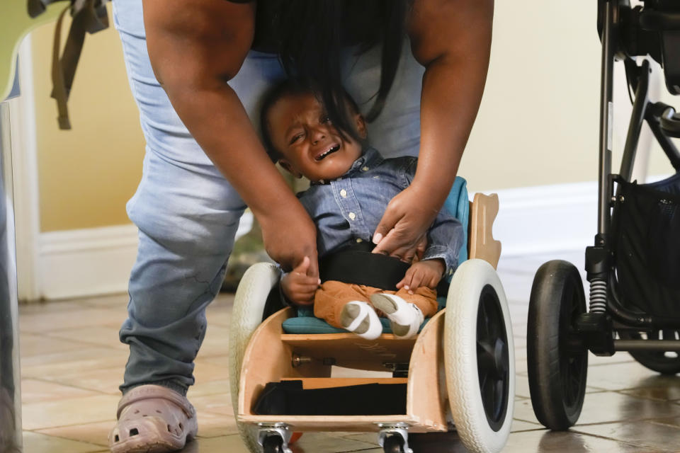 Crystal Jack straps her son Elijah Jack, 1, into his mobility chair, which was built as a donation by Tulane University students, at her home in New Roads, La., Thursday, Nov. 30, 2023. Tulane science and engineering students are making the second batch of mobility chairs for toddlers, that will eventually go to pediatric patients at Children's Hospital. Wheelchairs are expensive, and insurance won't cover the cost for children unless the child proves they can operate it independently. (AP Photo/Gerald Herbert)