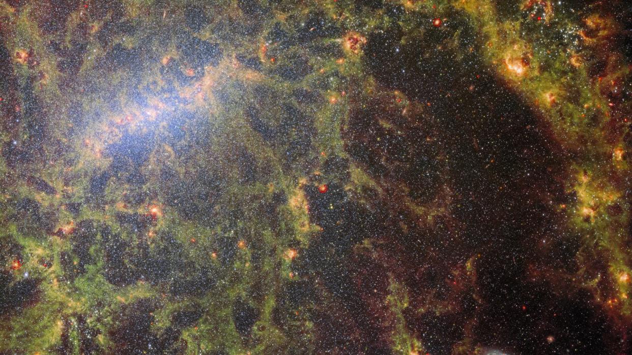  a dense field of stars overlaid with yellowish tendrils of gas 