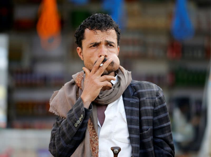 Man smokes a cigarette as he chews qat, a mild stimulant, at a fruit market amid concerns of the spread of the coronavirus disease (COVID-19) in Sanaa