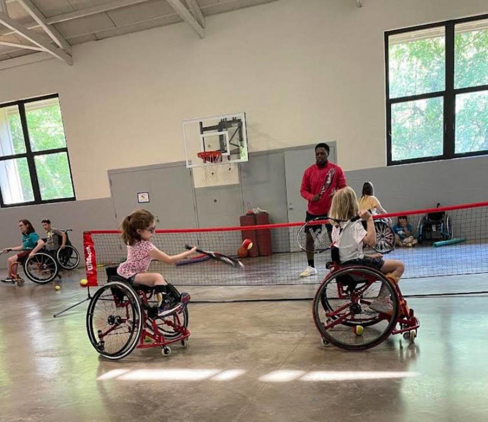 Two girls in wheelchairs learn how to play tennis.