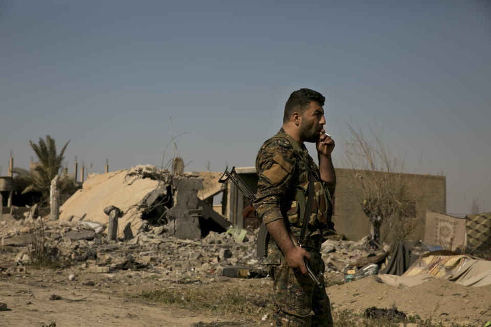 A U.S.-backed Syrian Democratic Forces (SDF) fighter smokes in a tent encampment that had been occupied by Islamic State group militants, in Baghouz, Syria, Monday, March 11, 2019. SDF forces made slow advances Monday into the edges of the last village held by IS, battling militants holed up in underground tunnels, a spokesman for the force said. (AP Photo/Maya Alleruzzo)
