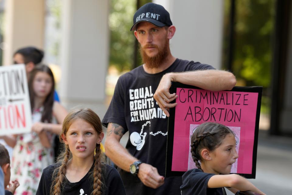 Abortion opponent Alexander Wirth, center, stands with two of his children outside the South Carolina Statehouse on Thursday, July 7, 2022, in Columbia, S.C. Protesters clashed outside a legislative building, where lawmakers were taking testimony as they consider new restrictions on abortion in the wake of the U.S. Supreme Court's decision overturning of Roe v. Wade. (AP Photo/Meg Kinnard)