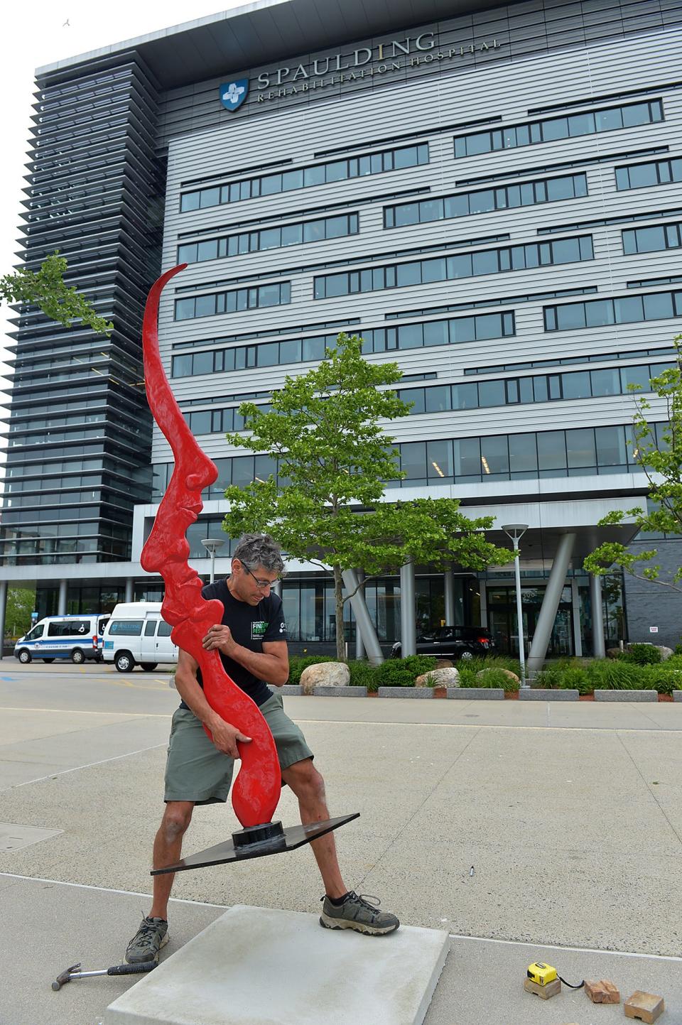 In front of Spaulding Rehabilitation Center, sculptor Michael Alfano of Hopkinton installs Self Reflection, one of 20 sculptures in the "Of Many Minds" waterfront exhibit at the Charlestown Navy Yard, June 16, 2022. The exhibit is scheduled to run through December 2023.