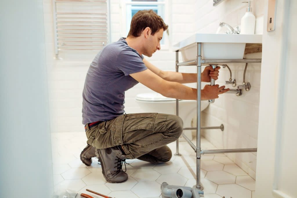 A man does plumbing work underneath a sink. 