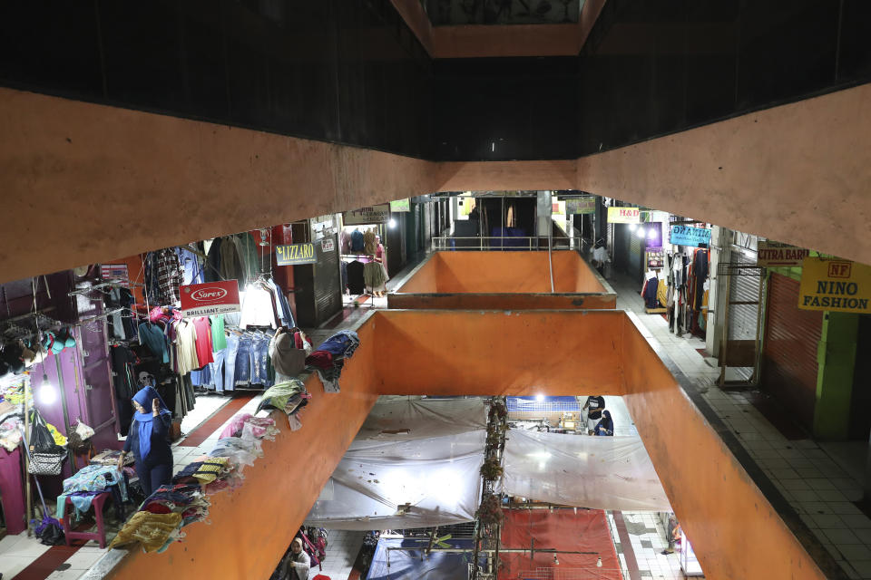 A woman walks near a shop at a quiet market in Jakarta, Indonesia, Friday, April 10, 2020. Authorities began stricter measures to halt the new coronavirus' spread in Indonesia's capital Friday, with its normally congested streets empty after death toll spiked in the past week. (AP Photo/Achmad Ibrahim)