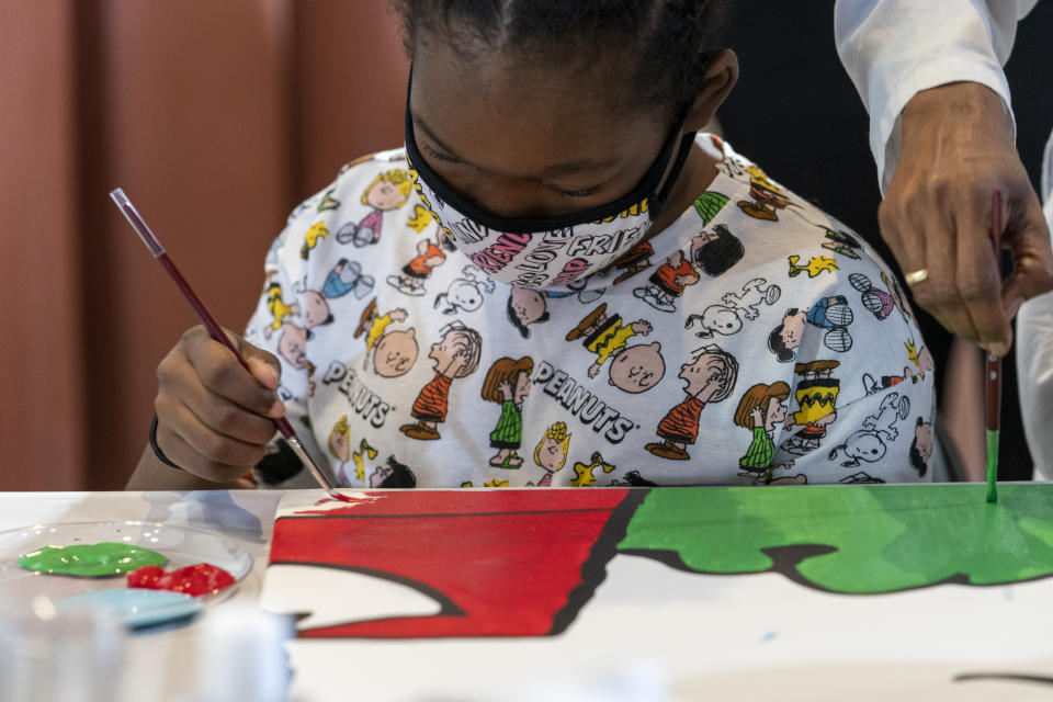 Kerrin McCarthy, 14 , paints a panel of a "Peanuts" mural that will be placed in the outpatient pediatric floor of One Brooklyn Health at Brookdale Hospital, Thursday, Oct. 1, 2020, in the Brooklyn borough of New York. The beloved comic marks its 70th anniversary this week with new lesson plans, a new TV show and a philanthropic push that includes donating "Peanuts" murals for kids to paint in 70 children's hospitals around the globe, from Brooklyn to Brazil.(AP Photo/Mary Altaffer)