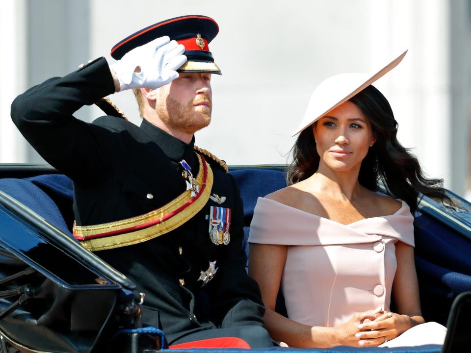 Meghan Markle looks at Prince Harry as he salutes.