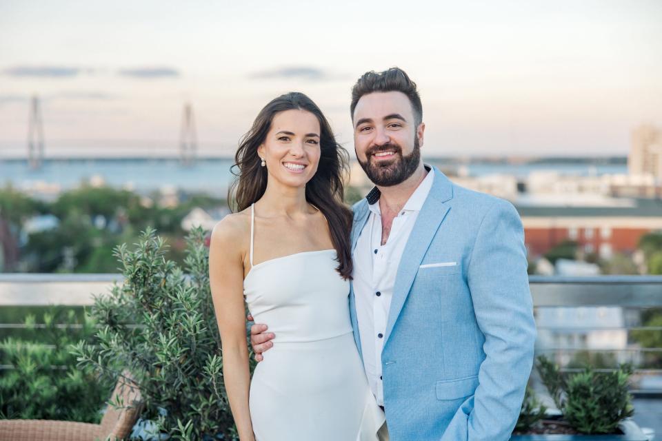 A bride and groom smile in front of a sunset.