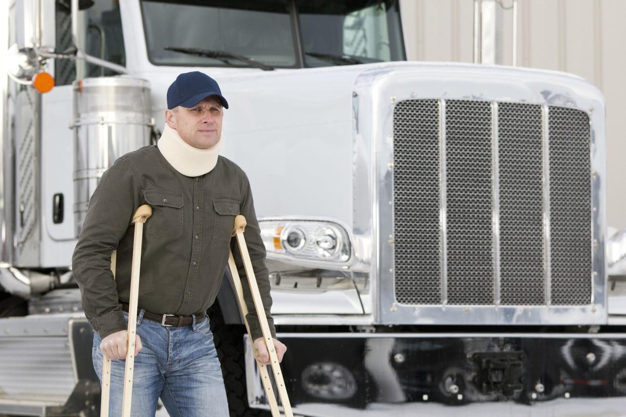 truck driver standing with crutches in front of truck