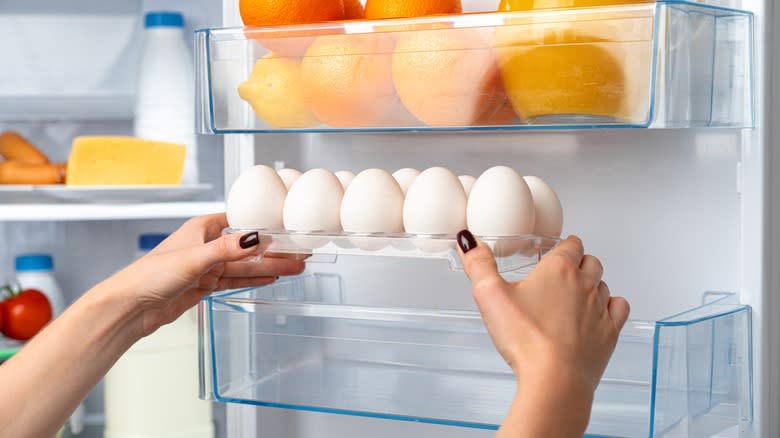 person putting eggs in fridge door