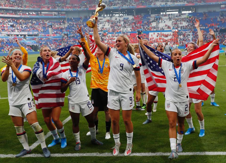 Lindsey Horan hoists the World Cup while surrounded by her USWNT teammates.