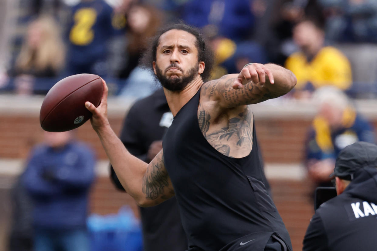 Colin Kaepernick, in black, with tattoos on his upper body and upper arms, throws a pass.