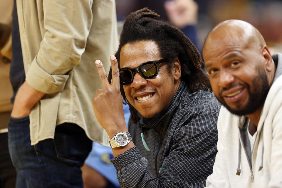 American rapper Jay-Z wearing a Black jacket a basketball game posing for a picture, peace sign.