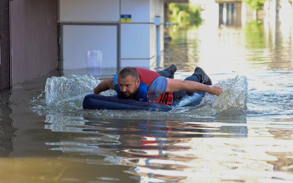 A local resident is seen on an inflatable mattress in a flooded area in Kherson - OLEXANDER KORNYAKOV/AFP