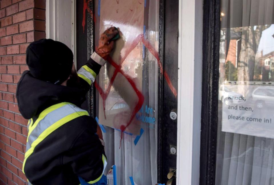 A graffiti removal worker cleans anti-Semitic graffiti, including a swastika, that was spray painted on the door of The Glebe Minyan in Ottawa, on Tuesday, Nov. 15, 2016. The federal government is making it easier for religious and cultural groups at risk of hate crimes to improve security in and around their buildings.