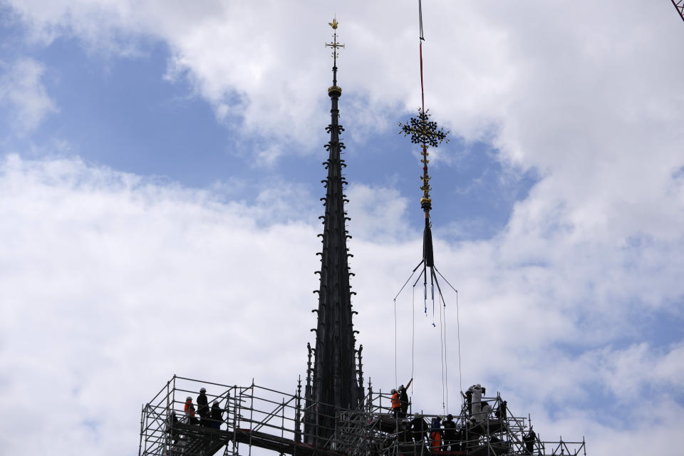 Workers install Notre Dame de Paris cathedral's Croix du Chevet in front of the cathedral spire, left, to be reinstalled Friday, May 24, 2024, in Paris. The Croix du Chevet is the only piece of the cathedral roof that did not burn in the devastating April 2019 fire. (AP Photo/Thibault Camus)