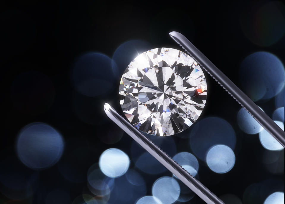 A sparkling round-cut diamond held in a jeweler's tweezers.