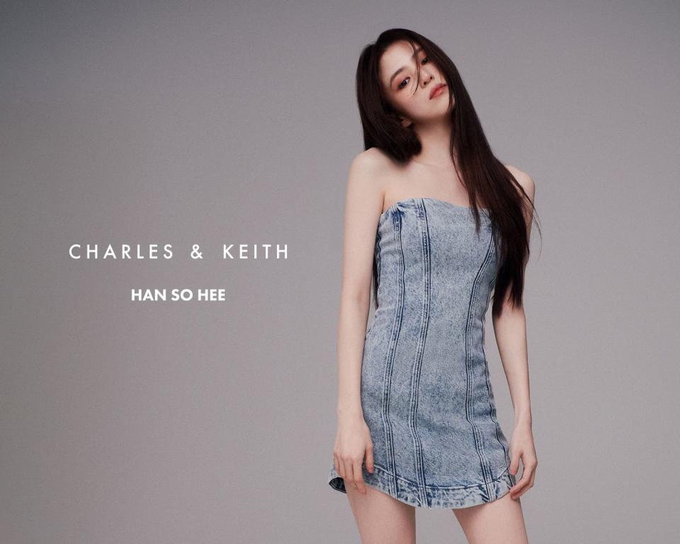 Han So-hee stands in a denim dress with long hair flowing. 